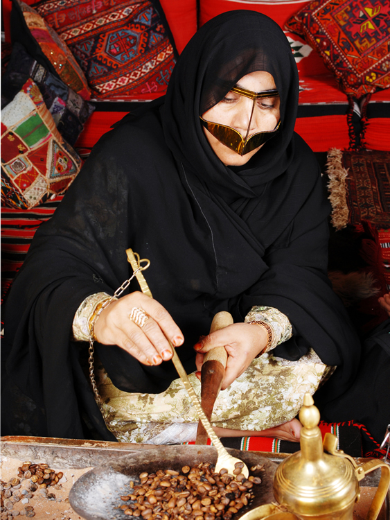 An Emarati woman wearing the traditional burqa (face mask) roasting  Arabic coffee beans using Al-Mehmas and Al-Migla (a copper stir and a pan, tools for roasting Arabic coffee) while participating in an Arabic coffee making competition.