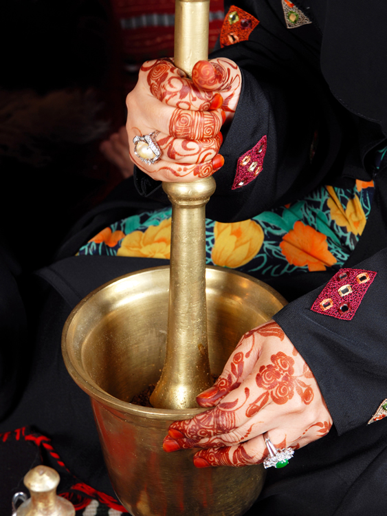 An Emarati Woman wearing henna grinds the Arabic coffee using Al-Minhaz (Grinder)