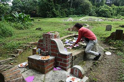 A devotee preparing offerings at a grave during the Qing Ming Festival prior to COVID-19