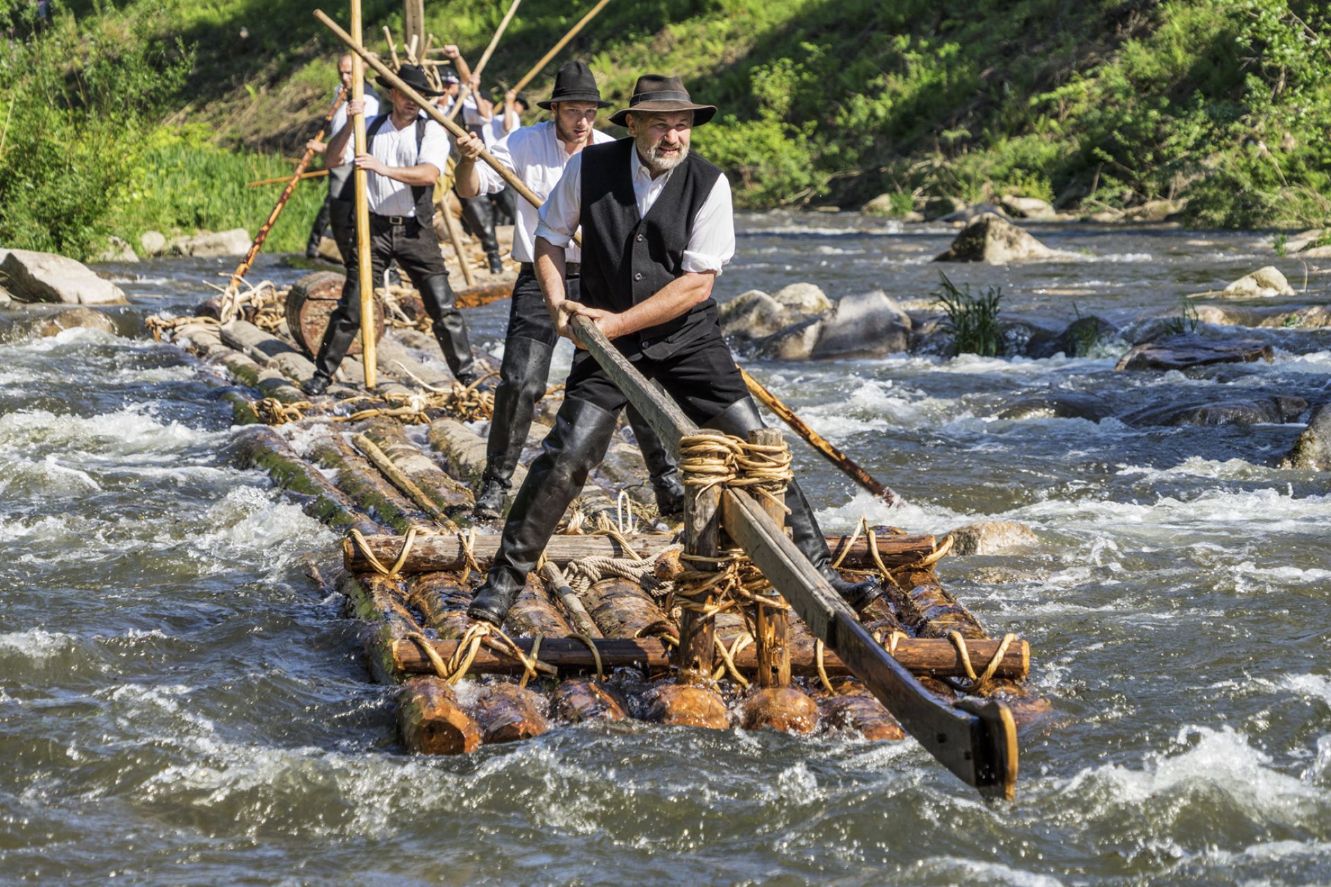 Younger and older rafters are concentrated while steering the timber raft on the wild river, Germany
