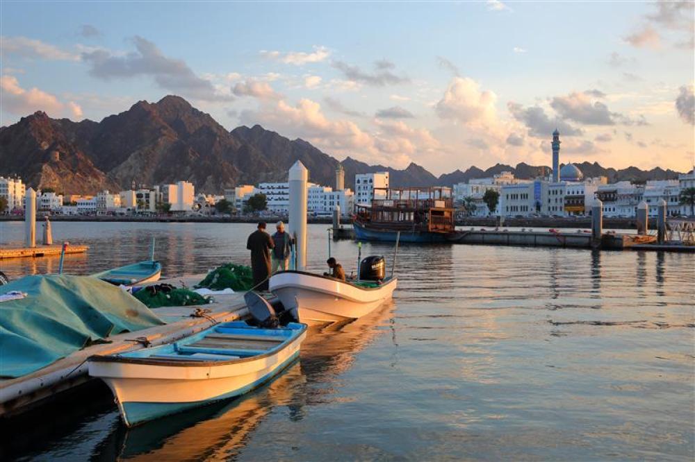 MUTTRAH, MASCATE, OMAN - 26 DÉCEMBRE 2024 : La jetée près du marché aux poissons au coucher du soleil, avec les pêcheurs qui travaillent sur leurs filets de pêche, et avec la corniche de Muttrah en arrière-plan